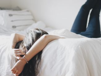 Eine junge Dame mit dunkelbraunen Haaren liegt auf einem weißen Bett