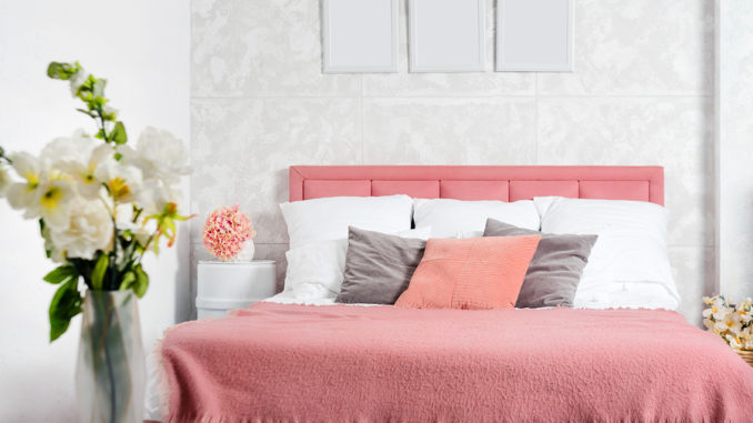 Stilvoller Innenraum des modernen Schlafzimmers. Weißes und rosa Design des gemütlichen Schlafzimmers mit Blumen. Kingsize-Bett mit rosa und grauer Bettwäsche