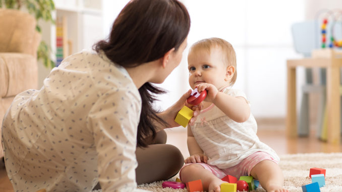 Nettes Baby, das mit pädagogischen Spielwaren in der Kindertagesstätte spielt. Kind, das Spaß mit bunten verschiedenen Spielwaren zu Hause hat. Kindermädchen kümmert sich um Kindkleinkind.